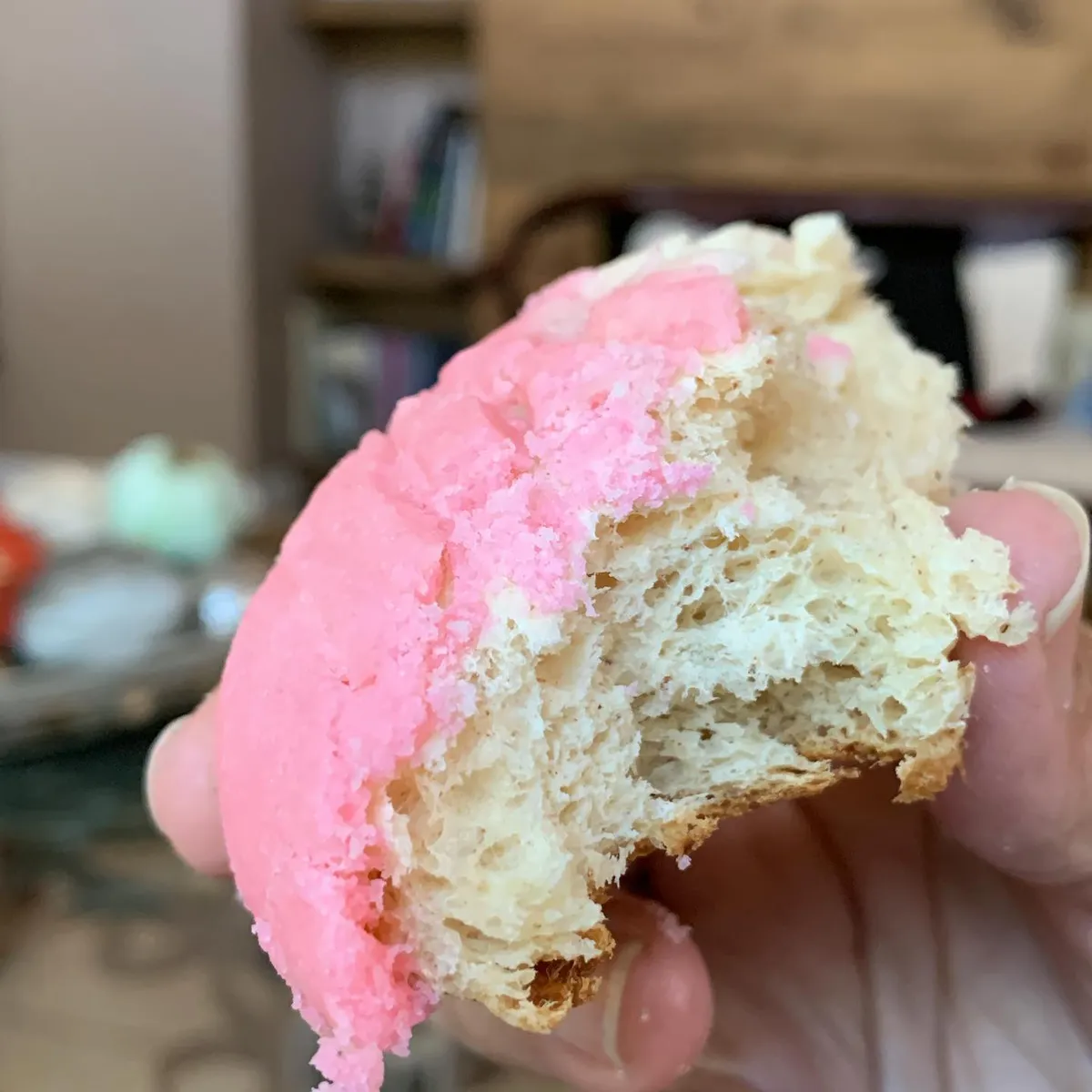 A pink concha with a bite taken, showing the soft, fluffy bread inside