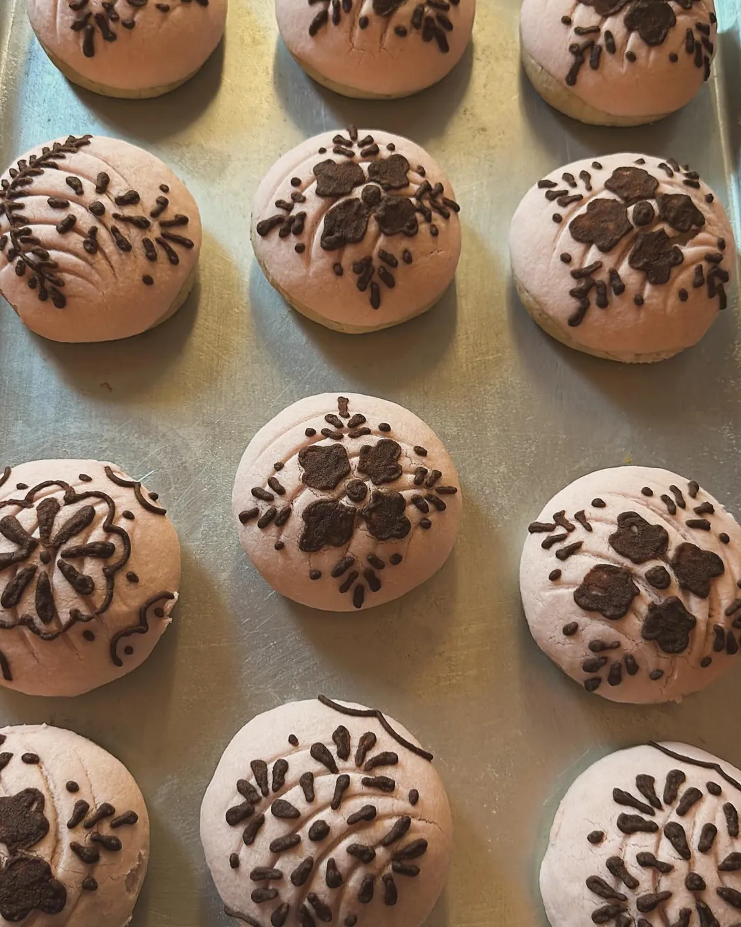 Blush conchas with delicate chocolate lace designs on a baking tray