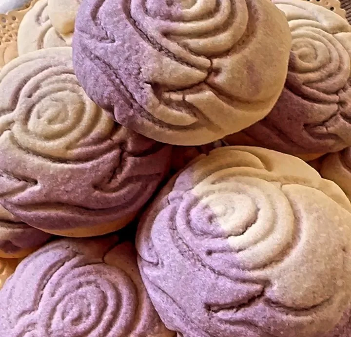 A stack of lavender and vanilla rose-swirl conchas on a lace doily